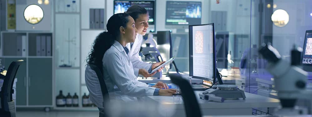 Pair of researchers in lab coats typing on computers in lab setting