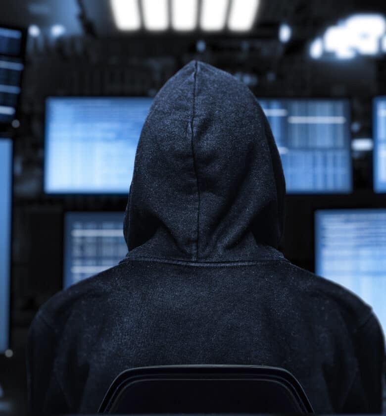 A person in a hoodie standing in front of computer screens