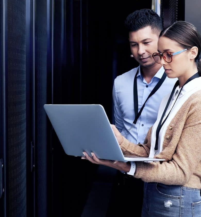 Two individuals standing in front of a server, one holding a laptop